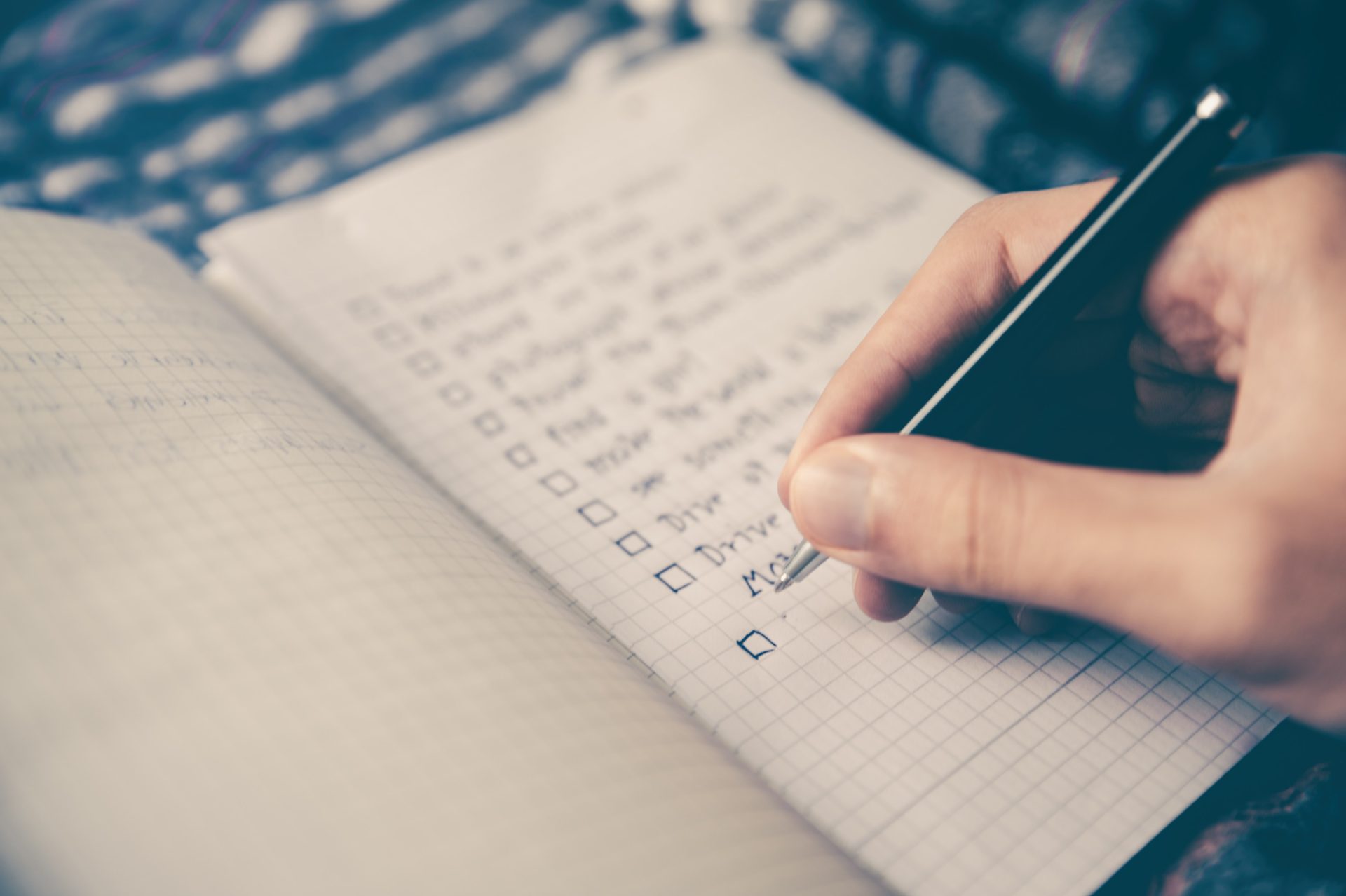 A person's hand writing a checklist in a notebook